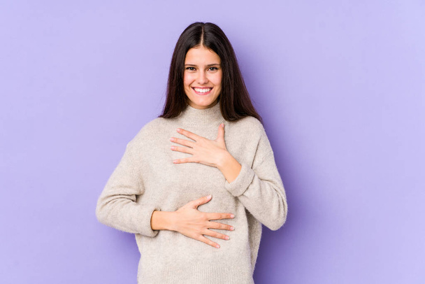 Young caucasian woman isolated on purple background laughs happily and has fun keeping hands on stomach. - Photo, Image