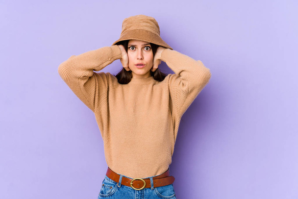 Young caucasian woman isolated on purple background covering ears with hands trying not to hear too loud sound. - Foto, Bild