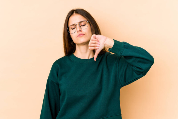 Young caucasian woman isolated on beige background showing a dislike gesture, thumbs down. Disagreement concept. - Foto, Bild