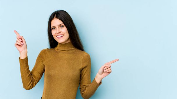 Young caucasian woman isolated on blue background pointing to different copy spaces, choosing one of them, showing with finger. - Photo, Image