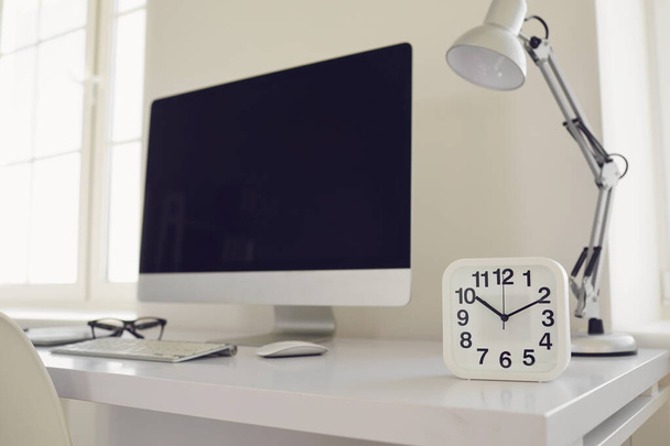 White modern workplace with windows computer alarm clock on the table - Фото, изображение