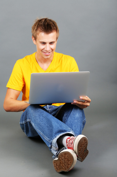 A handsome young man with laptop on grey background - Foto, immagini