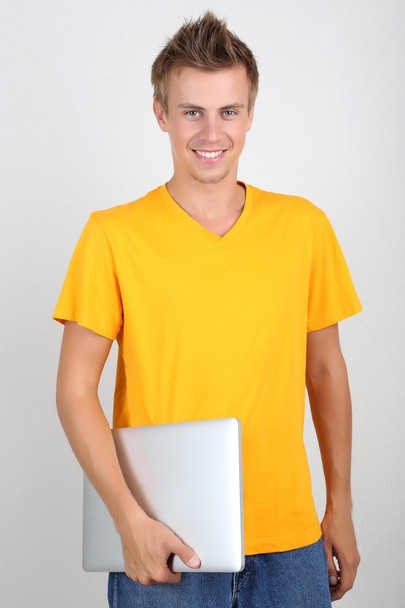 A handsome young man with laptop on grey background - Foto, imagen