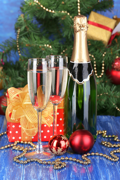 Bottle of champagne with glasses and Christmas balls on wooden table on Christmas tree background - Photo, Image