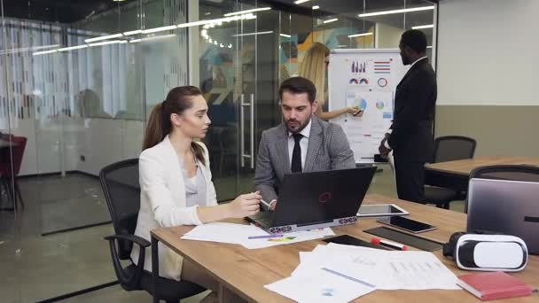 Close up of attractive serious high-skilled multiethnic business colleagues which working at the meeting table using computer and flip chart board - Кадры, видео
