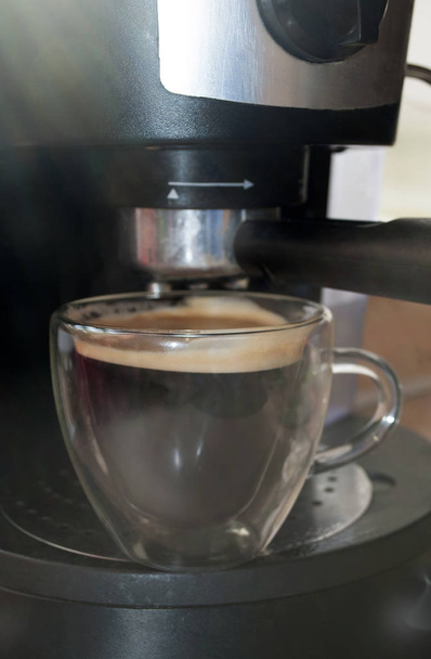 La cafetera. Muy cerca. Café en una taza de vidrio de doble pared. El café se vierte de una máquina de café en la mañana
 - Foto, Imagen