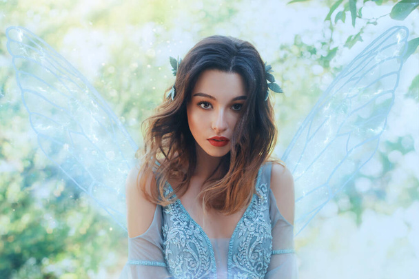 Fantasy closeup portrait attractive woman in image young fairy. carnival Costume blue dress transparent wings. face tender red makeup. Wavy Brunette hair Flutter fly in wind. Green nature backdrop - Zdjęcie, obraz