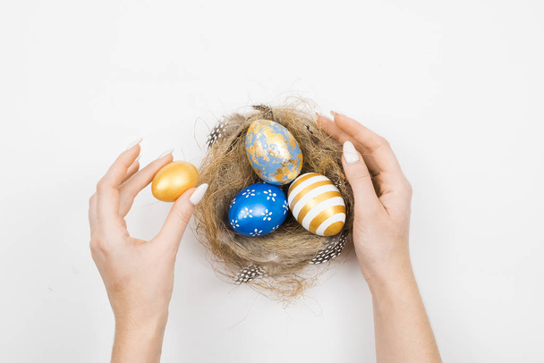Easter golden decorated eggs in nest with woman hands isolated on white background for web banner. Minimal easter concept. Happy Easter card with copy space for text. Top view, flatlay. - Foto, imagen