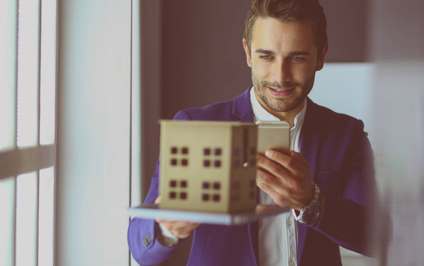 Businessman holding house miniature on hand standing in office. - Fotoğraf, Görsel