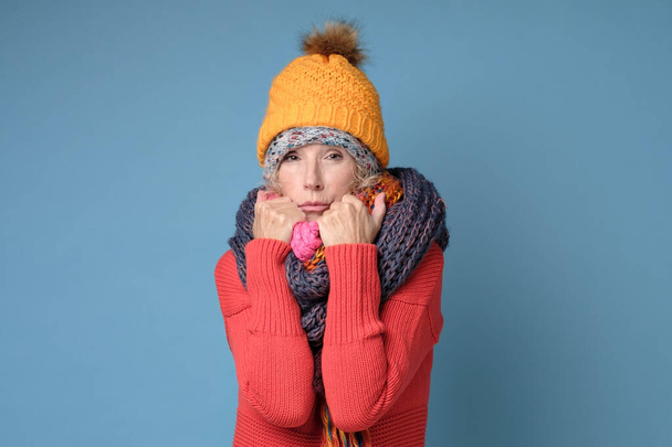 Frozen senior woman in hats and scarfs isolated on blue wall. - Photo, Image