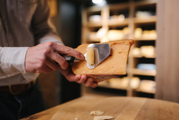 Człowiek krojący kawałek sera dla smaku. Młody pracownik używa specjalnego noża do sera - Zdjęcie, obraz