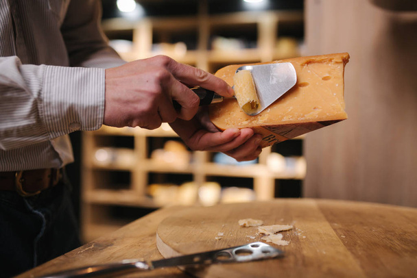 Az ember kis sajtot szeletel ízlés szerint. Fiatal munkavállaló speciális kést használ sajt - Fotó, kép