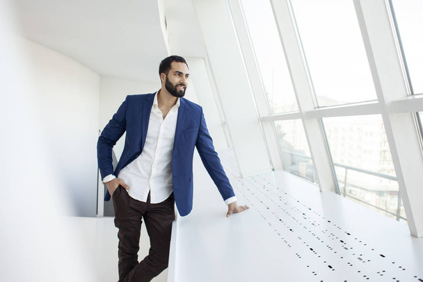handsome successful company manager stands in a white office and looks out the window, portrait of a businessman at the workplace - Photo, Image