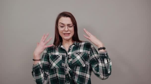 op grijze achtergrond geïrriteerde vrouw met bril schudt haar handen - Video