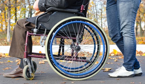 Homem deficiente em uma cadeira de rodas com um cuidador
 - Foto, Imagem