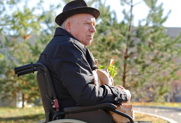 Homem idoso em uma cadeira de rodas desfrutando do sol
 - Foto, Imagem