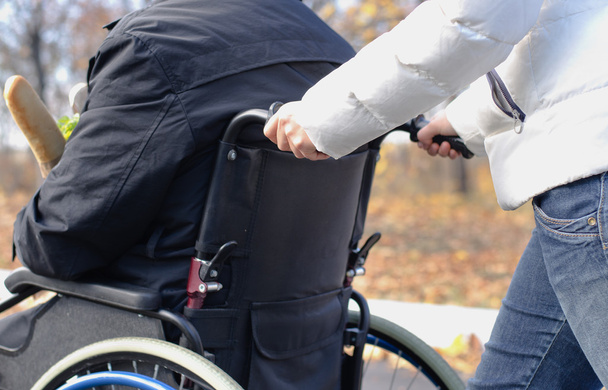 Nainen työntää vammaista miestä pyörätuolissa
 - Valokuva, kuva