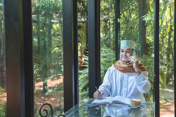 Arabe musulman homme d'affaires utilisent la communication smartphone et écrire sur le livre dans un café, freelance aucun mode de vie espace de travail
. - Photo, image