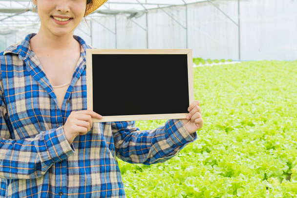 緑のレタス農場の横に立つアジアの男女の一部を背景にした低原性有機農場の緑野菜に空の小さな黒板、中小企業の起業家の概念 - 写真・画像
