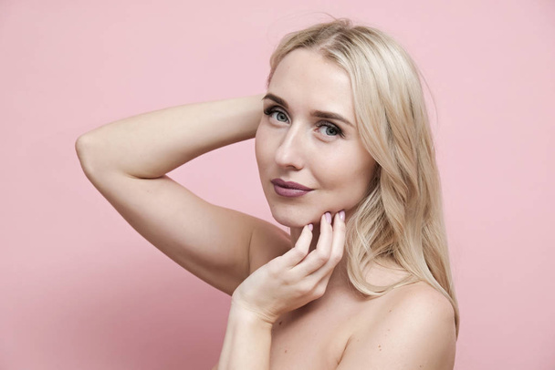 Beautiful blond woman with naked shoulders on pastel pink background. Beauty, cosmetics and skin care concept - Foto, immagini