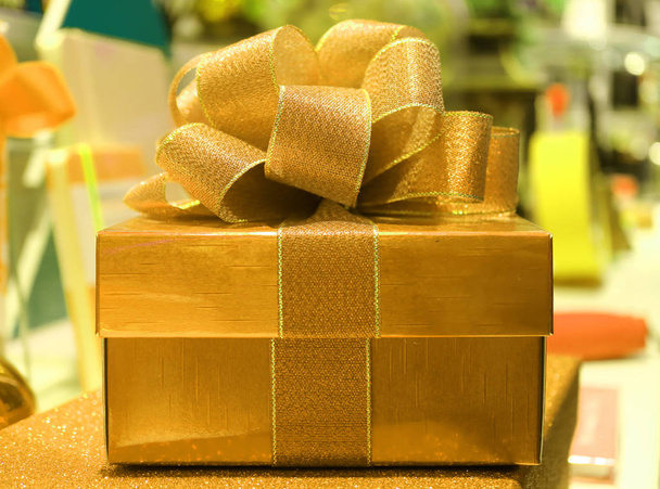 Vista frontal de uma caixa de presente de ouro brilhante quadrado com arco de fita de ouro Glitter, fundo borrado - Foto, Imagem