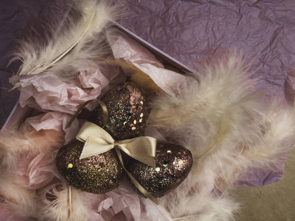 Paaseieren in een roze geschenkdoos met veren, paasversiering. Nest met gouden rode eieren op feestelijke achtergrond Wenskaart. Vrolijk Pasen. - Foto, afbeelding
