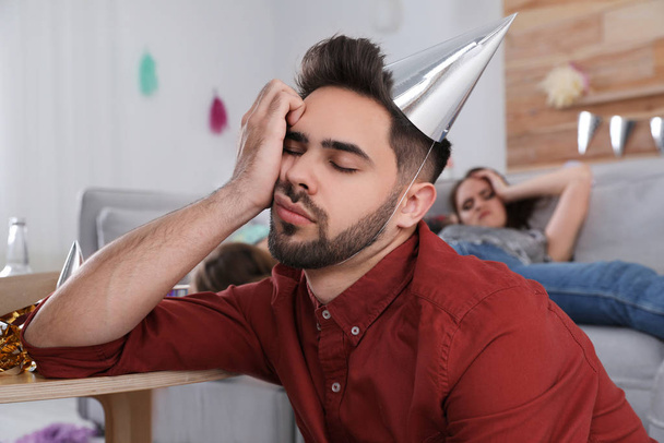 Young man with festive cap sleeping at table after party - Photo, Image