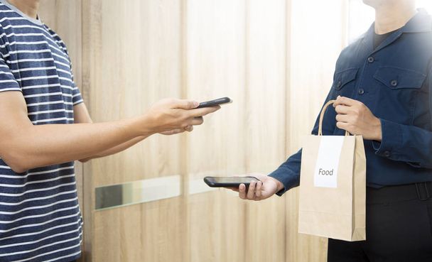Человек получает еду в бумажном пакете доставки с помощью сканирования смартфона платить
 - Фото, изображение