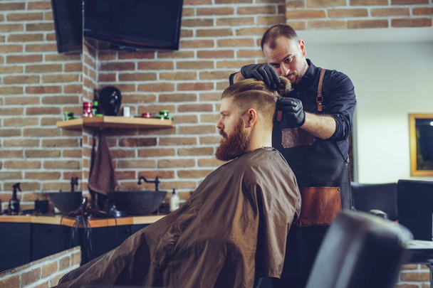 Creating new hair look. Young bearded man getting haircut by hairdresser. - Φωτογραφία, εικόνα