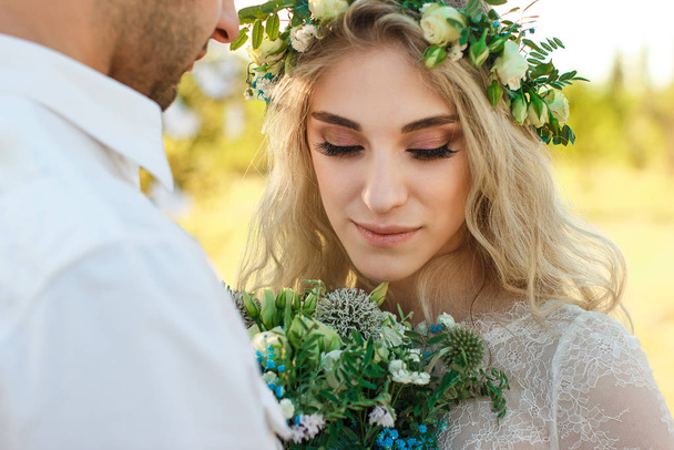 Bride in white dress and wreath and groom portrait in sunny summer day. Rustic outdoor wedding concept. Soft selective focus. - Foto, imagen