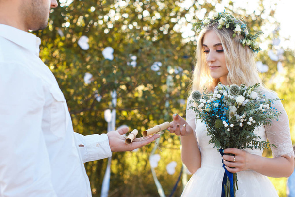 Voti nuziali su foglio di carta arrotolato sul palmo dello sposo, bouquet da sposa, concetto di matrimonio all'aperto rustico
. - Foto, immagini