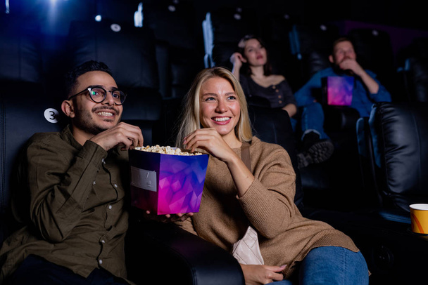 Веселая молодая пара, проводящая время в кино, поедая кукурузу и наслаждаясь просмотром фильма - Фото, изображение