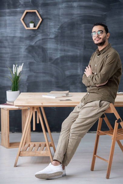 Fiatal magabiztos üzletember vagy irodai dolgozó keresztbe karok mellkason, miközben áll az asztalnál a háttérben a táblán - Fotó, kép