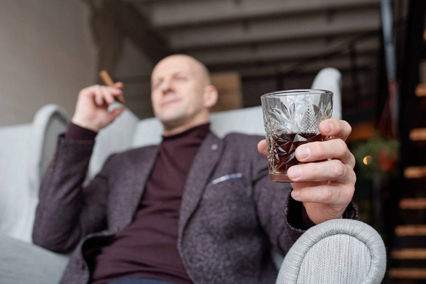 Az alábbi nézet üzletember zakóban ül karosszékben, miközben szivarozik és alkoholt iszik - Fotó, kép