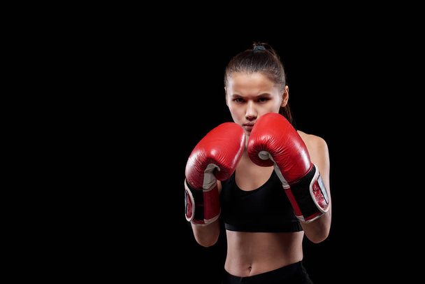 Młoda, poważna i potężna kobieta w odzieży aktywnej i rękawiczkach bokserskich, gotowa do walki na czarnym tle - Zdjęcie, obraz