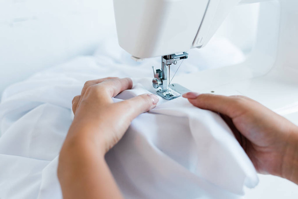 Cierre de la mujer inreconocible ajustando el tejido blanco bajo la aguja de la máquina de coser. - Foto, Imagen