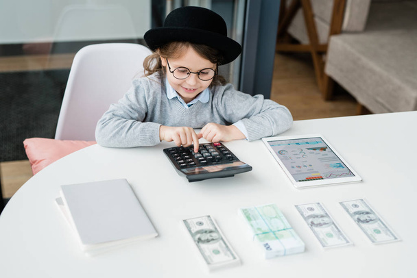 Mały księgowy korzystający z kalkulatora podczas liczenia pensji lub pieniędzy i dokonywania analizy finansowej przez biurko - Zdjęcie, obraz