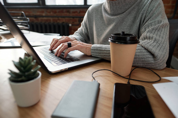 Крупним планом невпізнавана бізнес-леді, сидячи за столом з чашкою кави і редагуючи файли на ноутбуці
 - Фото, зображення