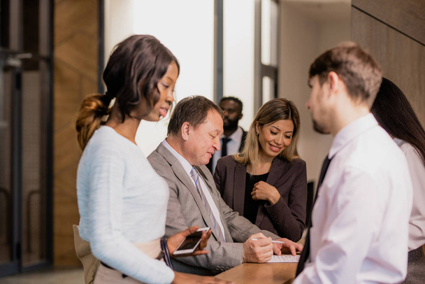 Grupo de empresários contemporâneos de diversas etnias e idades comunicando por balcão de recepção no hotel - Foto, Imagem