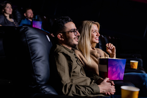 Happy young amorous couple relaxing in cinema in front of large screen while enjoying love story movie - Photo, Image