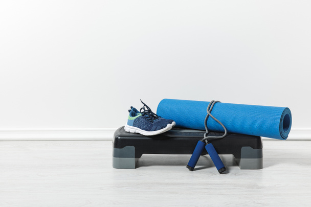 step platform, blue fitness mat, jump rope and sport shoes on floor at home  - Foto, Imagem