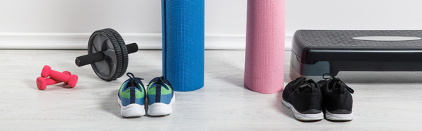 tiro panorâmico de tapetes de ioga, tênis, plataforma de passo e equipamentos esportivos no chão em casa
  - Foto, Imagem