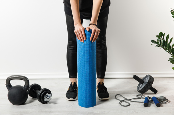 cropped view of sportswoman standing with fitness mat at home with sport equipment - Photo, Image