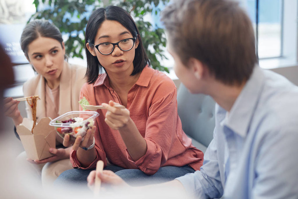 Ryhmä nuoria liikemiehiä, jotka syövät noutoruokaa ja juttelevat lounastauolla toimistossa, kopioivat tilaa
 - Valokuva, kuva