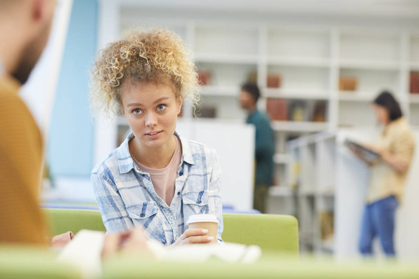 Портрет девочки-подростка, разговаривающей с партнером за столом во время учебы в библиотеке колледжа, копировальное пространство
 - Фото, изображение