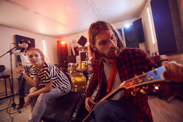 Fisheye portrait of handsome long-haired man playing guitar with contemporary music band during rehearsal or concert in studio, copy space - Foto, Imagem