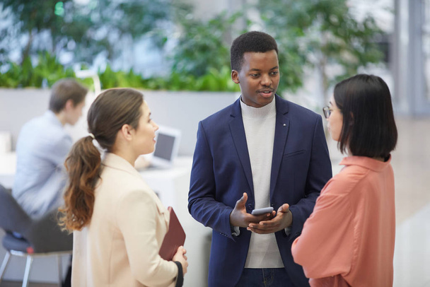 High angle view at multi-ethnic group of business people talking while standing in modern office interior, focus on successful African businessman talking to two women - Photo, Image