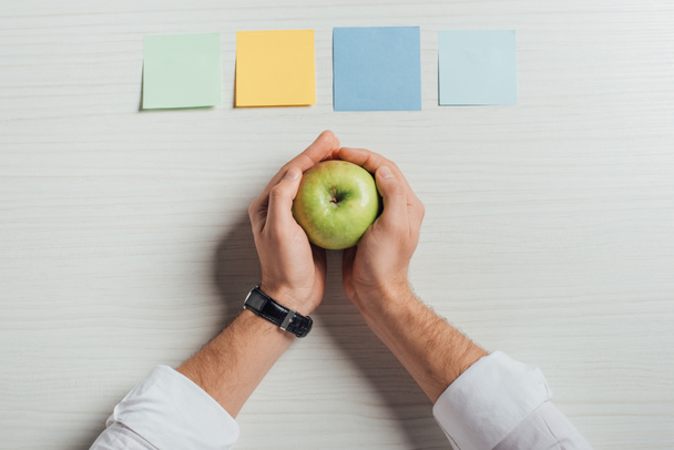 partial view of businessman holding apple on table with note stickers - Photo, Image