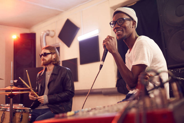 Retrato del hombre afroamericano contemporáneo cantando al micrófono y sonriendo felizmente durante el ensayo o concierto en el estudio de música, espacio para copiar
 - Foto, imagen