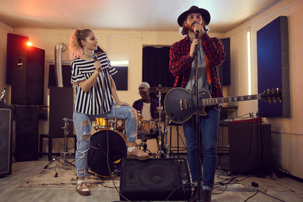 Full length portrait of contemporary music band enjoying singing with beautiful woman and bearded guitarist in foreground, copy space - Photo, Image